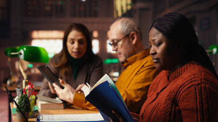 African american woman asking people for silence in a public library, being disturbed by their collective studying with a lot of noise.の写真素材