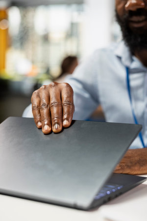African American individual at office desk opening laptop, ready for corporate meeting and daily work tasks. Close up of hands of black man on digital device, preparing for report writing.の写真素材