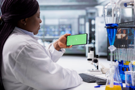Black expert using chroma key screen for laboratory study on smartphone, works with experiment data for molecular science. Advanced research, pharmacology and biotechnology discovery.の写真素材
