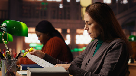 Female person with a focused expression highlighting important ideas from class notes, reading files at college library. Academic research to complete her degree. Self growth.の写真素材