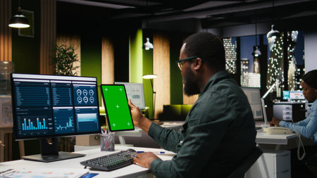 Green screen on tablet next to young black businessman reviewing data, working on analytics report...