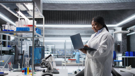 Black female researcher in a clinical research lab studies experiment data with a laptop. Showcasing biotechnology, genetics research and pharmacology for progress in healthcare.の写真素材