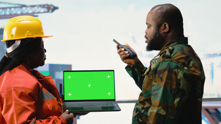 Chroma key laptop used by soldier on offshore platform communicating via military radio. Naval unit on drilling barge using green screen mockup notebook, speaking on walkie talkieの写真素材