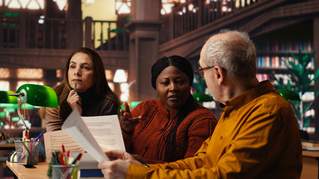Mature team of performers rehearsing script dialogue together in a library, making drama play role...
