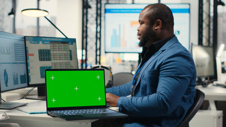 Black analyst uses computer to analyze charts with chroma key on laptop, preparing strategy reports...