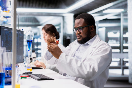 Chemical engineer in lab inspecting chemical compound clarity in vials for purity verification. African american man in research facility doing RD, preparing reagent test tubes for assay proceduresの写真素材
