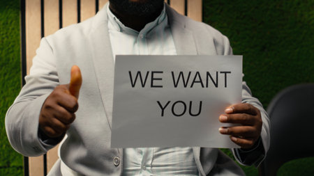 African american HR staff holding paper signs with hiring messages, announcing job openings and inviting skilled candidates to join the company workforce. Workplace culture advertisement.の写真素材
