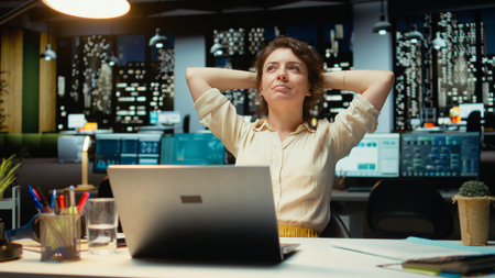 Pleased businesswoman enjoys a quiet moment of downtime in a corporate setting, reclining in her chair with comfortable laid back posture. Resting after tasks, radiates empowerment. Camera A.の写真素材