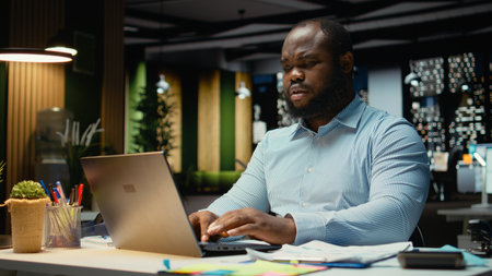 Male african american worker reading emails and handles management tasks, documenting insights for a...