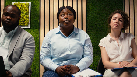 Anxious diverse job seekers awaiting job interview discussion with manager, showcasing anticipation in office hallway. People preparing with information for the recruitment process. Camera A.の写真素材