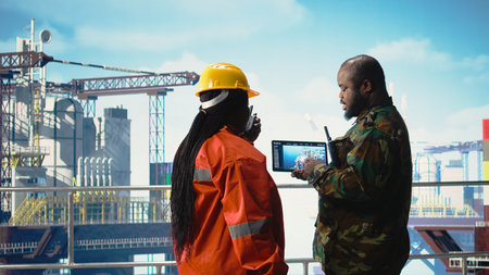 Soldier on offshore platform deck talking with technician, using device visualization software. African american naval unit guards drilling rig using tablet app,の写真素材