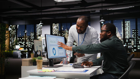 African american workers team consulting each other in solving tasks at night, completing monthly...