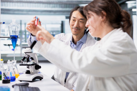 Smiling researchers in lab inspecting liquids in test tube, looking for breakthroughs during clinical trials. Happy research facility employees comparing chemicals vials, pleased to find right formulaの写真素材