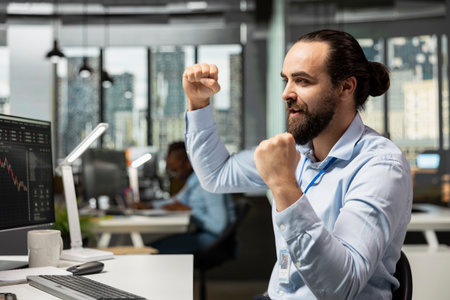Happy trader in prop firm office celebrating after winning money while executing trades using trading app on PC. Cheerful man delighted after seeing portfolio value increase while monitoring stocksの写真素材