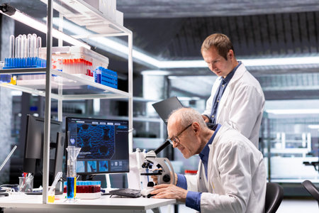 Experienced researchers using microscope optics in a lab research study. Sliding the sample tray for...