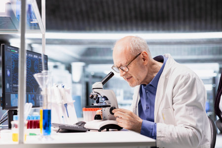 Old man scientist using microscope instrument in clinical research study. Sliding the sample tray for cellular investigation and supporting genetics research, advanced analysis for healthcare.の写真素材