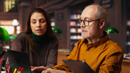 Multiethnic colleagues team writing class notes at the library, studying and reading in the college campus. Working together on learning and preparing for their thesis.の写真素材