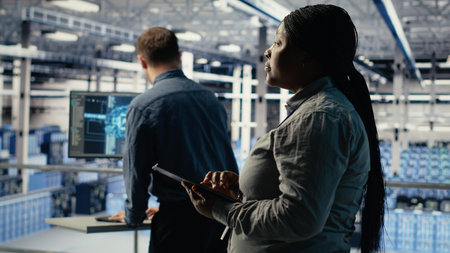 Team of data center technicians checks AI dashboard using laptop during systems review. Teamworking server hub colleagues test artificial intelligence tools on notebook, camera Bの写真素材