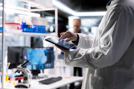 Male researcher conducts advanced research in microbiology on tablet, laboratory workspace features data analysis and biotechnology equipment. Healthcare innovation and medical research.の写真素材