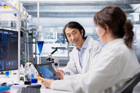 Smiling laboratory scientists using tablet app to process DNA patient data for clinical research. Upbeat lab colleagues use touchscreen device to do lab genetic analysis diagnosticsの写真素材