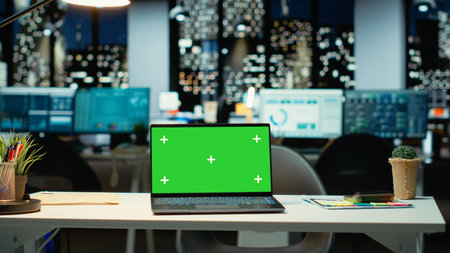 Empty corporate workspace with a green screen laptop in a multinational company late at night. Boardroom office set with reports, strategy icons and projections, ready for development.の写真素材
