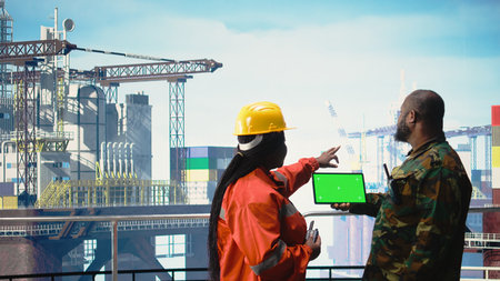 Chroma key tablet used by soldier on offshore platform deck talking with technician. African american unit guards drilling rig against threat using green screen mockup device.の写真素材