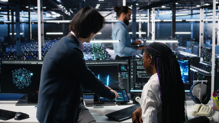 Multiethnic team in diverse data center coding with generative AI assistance. Asian man oversees work by IT expert leveraging artificial intelligence large language model, camera Aの写真素材