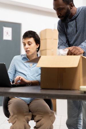 Two diverse staff members managing storage and order fulfillment, ensures hand packing and distribution for a small business. Employees team supporting local storehouse logistics.の写真素材