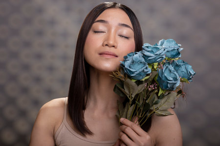Joyful female model with smooth skin and decorative flowers bouquet of blue roses, showing self confidence in studio. Empowering portrait celebrates body positivity and natural beauty.の写真素材
