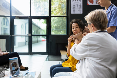 Asian patient receiving medical care for neck trauma from health staff, placing cervical brace for support during checkup. Medical team fixes spinal alignment for recovery in the waiting lobby.の写真素材
