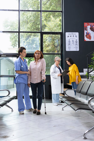 Patient walking with crutches during health check at modern hospital lobby, receiving assistance from nurse. Healthcare worker offering physical support while guiding recovery journey.の写真素材