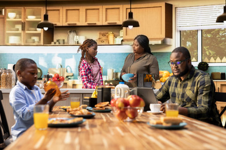 Father working on his laptop and serving breakfast with his cute family, gathered in the kitchen to enjoy the simple comfort of morning togetherness. Happy start to the day with sunlight.の写真素材
