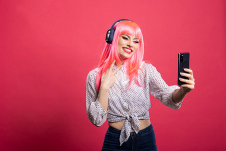 Cheerful woman with pink hair posing for selfie, flashing peace sign and making fun, cheeky face in...