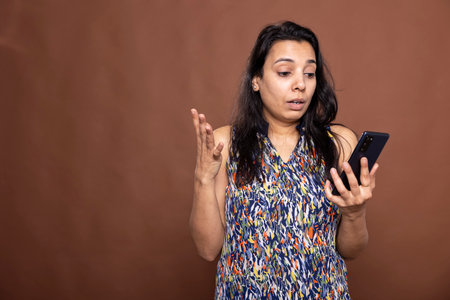 Portrait of attractive indian woman using mobile phone with surprised expression. Female individual...
