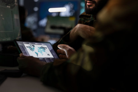 Military officer looking at surveillance footage on tablet, analyzing data to allocate resources to battlefield units based on mission needs. Army agent examining strategic data on device screenの写真素材