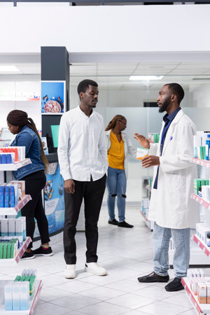 Healthcare worker recommending vitamin C supplements to a young man, assisting with medication instructions and advice at the pharmacy. Professional pharmaceutical service for wellness.の写真素材