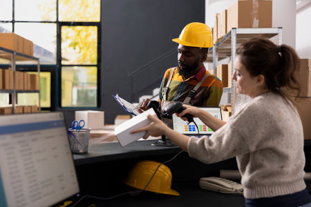 Multiethnic staff in coveralls checking parcels with a barcode scanner, managing storage inventory and supporting shipment service, e-shop logistics and small scale distribution for online orders.の写真素材