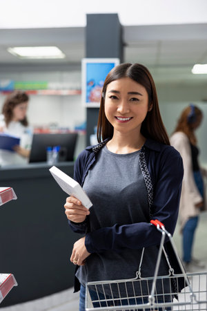 Portrait of smiling pharmacy client comparing biopharmaceutical products from shelves, focusing on wellness supplements treatment options in a professional retail healthcare environment.の写真素材