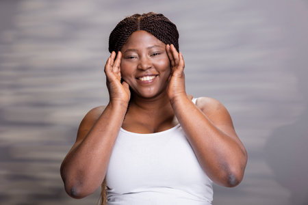 Black joyful woman showcasing glowing skin and natural makeup, positive soft feminine energy for beauty and self love advertisement. Empowering female vibrant model in the studio.の写真素材
