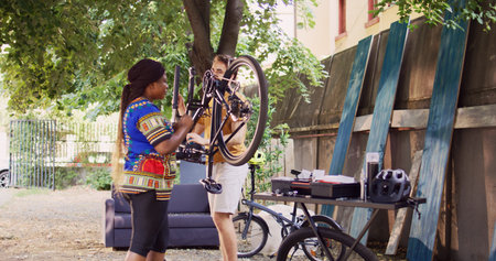 Athletic man safely dismantling damaged wheel from bicycle and helping young woman with further maintenance. Active couple meticulously repairing bike components.の写真素材