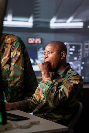 Tired military operative doing yawning gesturing after analyzing surveillance data during war. Counterintelligence agent feeling exhausted working night shifts during geopolitical operationの写真素材