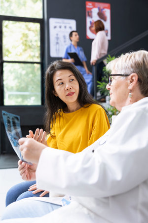 In a hospital lobby, healthcare worker provides assistance by explaining X ray results. Having a conversation in order to help with recovery plan and professional advice, preventive care.の写真素材