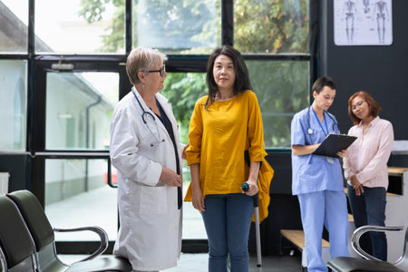 Medical expert helping Asian woman walk with mobility aid during routine hospital checkup. Specialist encouraging person to focus on injury recovery steps for independent movement.の写真素材