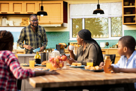 Parents and children starting the day with a healthy breakfast, cozy morning light in the kitchen. Family bonding, warmth and the joy of sharing delicious food together.の写真素材