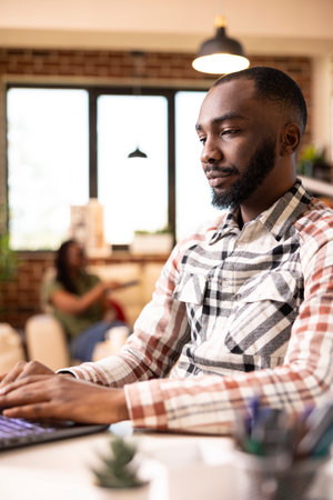 African american male manager typing on laptop, remotely replying to office emails and updating...