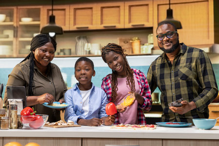 Portrait of cheerful parents cooking with kids to make homemade pizza together in a bright kitchen, spreading tomato sauce and layering pepperoni. Giving advice and tips to learn culinary hobby.の写真素材