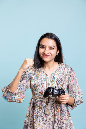 Indian jolly gamer winning the video gaming championship in studio, feeling confident and happy with her victory. Ecstatic woman entertained by video games on controller, enjoying leisure time.の写真素材