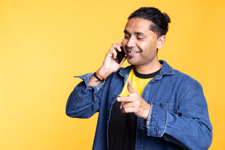 Upbeat indian person discussing with people during telephone call, casual clothing against orange...
