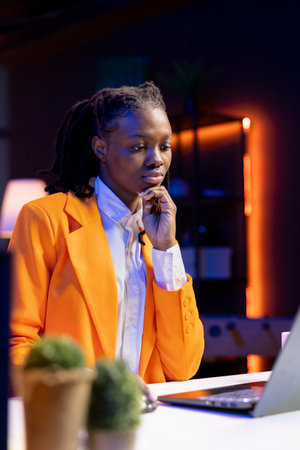 Freelancer in neon lit home office sitting at desk and typing on laptop keyboard. Remote employee using electronic device to do customers relations job online, answering inquiriesの写真素材