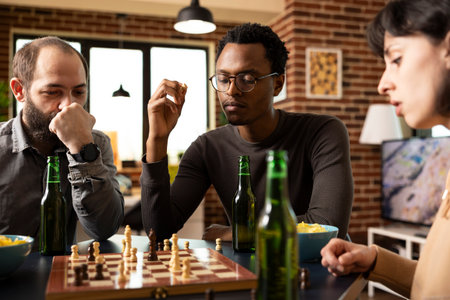 Multiethnic group of friends seated around table, enjoying a board game with snacks. African...